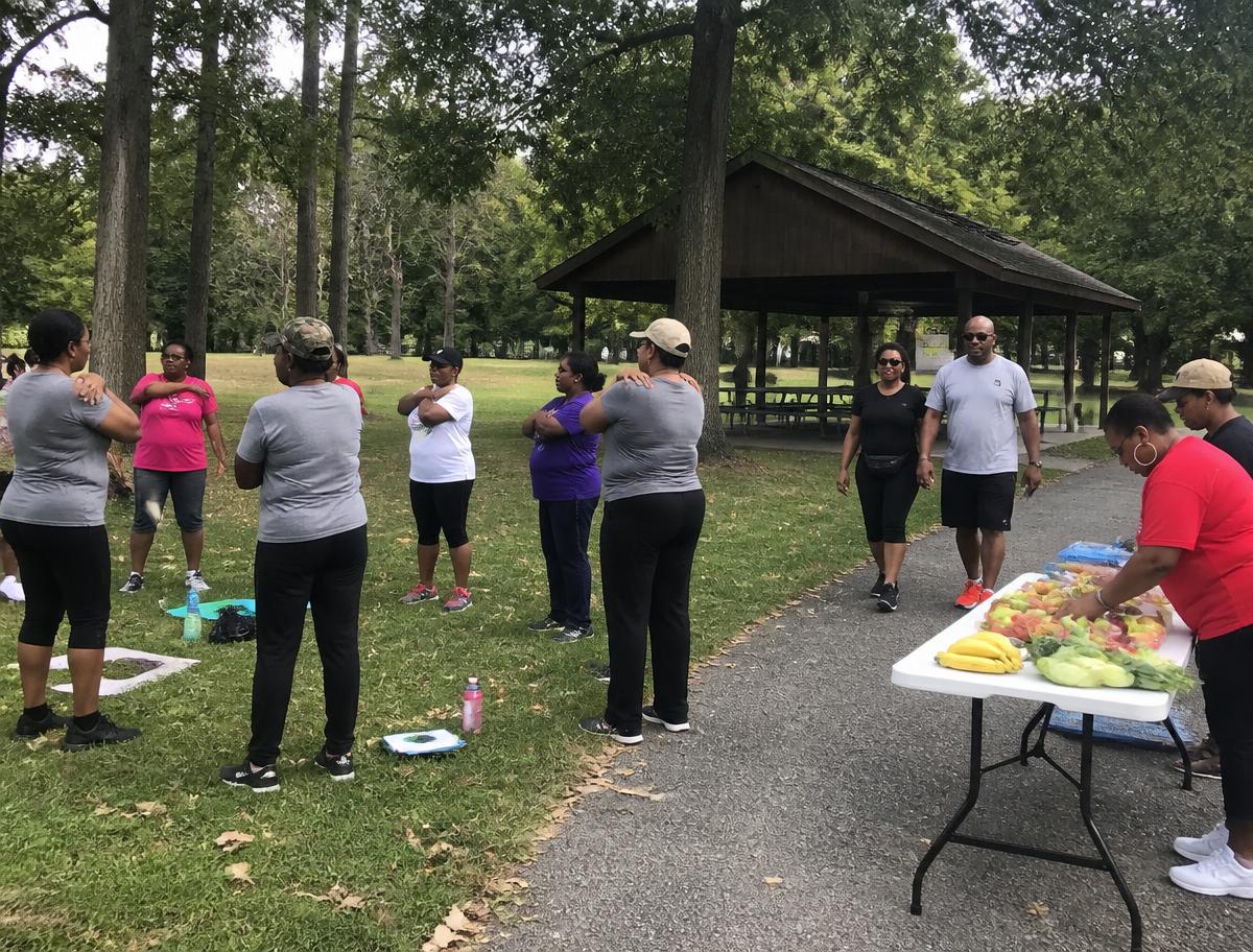 Diverse people of all ages engaging in healthy outdoor activities, including stretching, walking, and fresh produce sharing